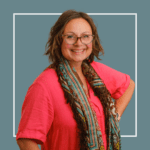 Grey background with white square outline with image of Professor Nancy Doyle, wearing a red t-shirt with a long brown patterned scarf, and glasses, smiling at the camera.