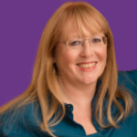 Lindsay smiling at the camera, wearing glasses and a teal blouse, with long, light auburn hair and a fringe, against a plain purple background.