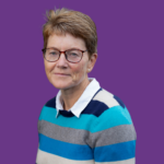 Professional headshot of Mandy Dennison, with short brown hair and glasses, wearing a blue, turquoise and grey striped jumper over a white collared shirt, against a purple background.