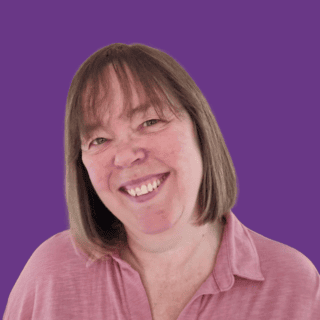 Theresa smiling at the camera, with shoulder-length light brown hair and a fringe, wearing a pink collared top against a plain purple background.
