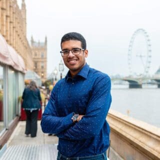 Profile of Lee chambers outside the Hours of Lords, folding arms and wearing a blue shirt.