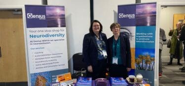 Photo of CEO Jacqui Wallis and Director of Operations Fiona Barrett at a conference stand with Genius Within leaflets, banners and branded free gifts.