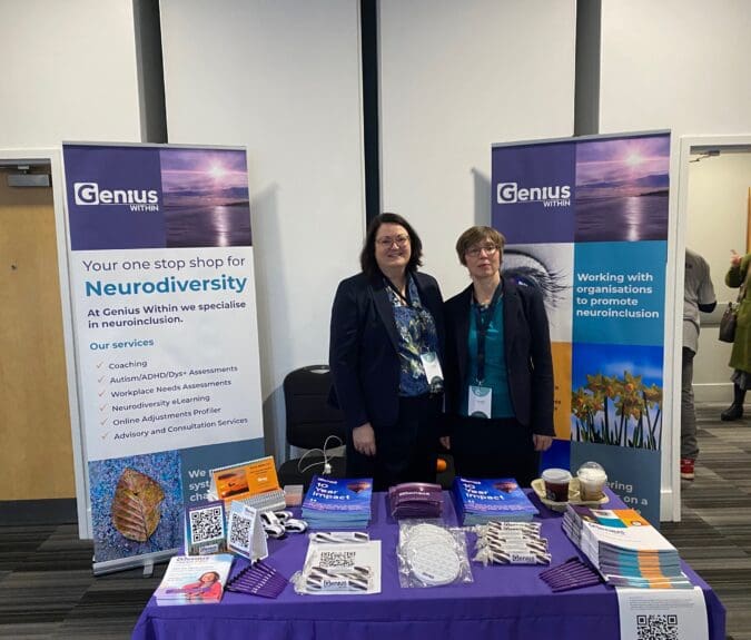 Photo of CEO Jacqui Wallis and Director of Operations Fiona Barrett at a conference stand with Genius Within leaflets, banners and branded free gifts.