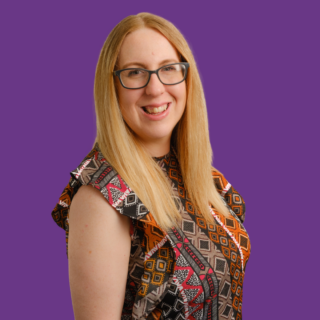 Zoe Farmer smiling in a professional portrait against a purple background, wearing glasses and a patterned sleeveless top.