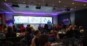 Awards stage adn room. atendees sat a tables with jacqui Wallis on stage opening the ceremony