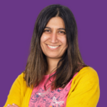 Professional headshot of Narinder Sheena smiling with long dark hair, wearing a yellow cardigan over a pink floral top, against a purple background