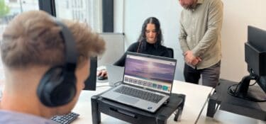 two men and a woman working at desks, one man is standing and helping the woman complete her neurodiversity awareness eLearning.