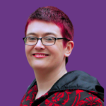 Head-and-shoulders portrait of Bex Harper with short dark hair dyed bright pink at the front, wearing rectangular black glasses and smiling at the camera. They are wearing a black and red patterned jacket with a black hood against a solid purple background.