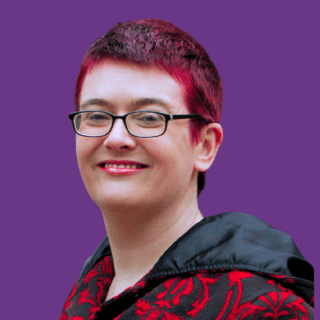 Head-and-shoulders portrait of Bex Harper with short dark hair dyed bright pink at the front, wearing rectangular black glasses and smiling at the camera. They are wearing a black and red patterned jacket with a black hood against a solid purple background.