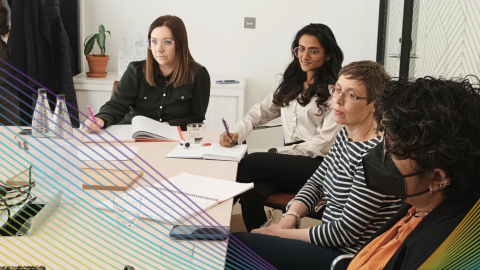 A group of people in a meeting room, taking notes and listening attentively.