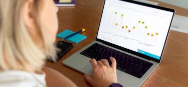 Photo is over the should of a person sat at a table with a laptop open. On the screen is a page showing a Genius Finder spiky profile