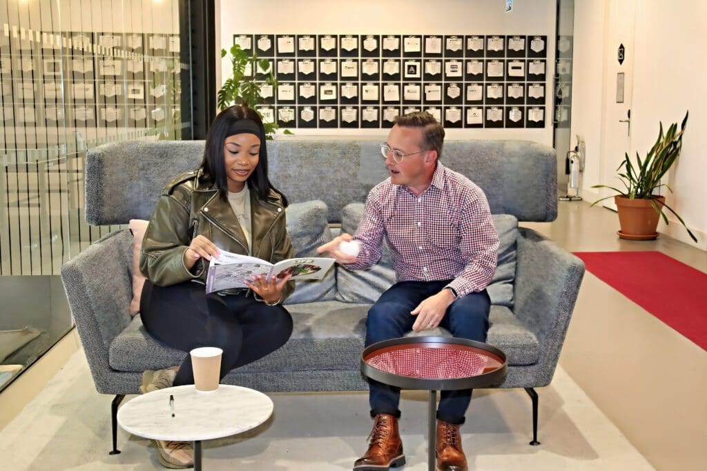 Two people in a discussion sat on a sofa. One of them holds a brochure