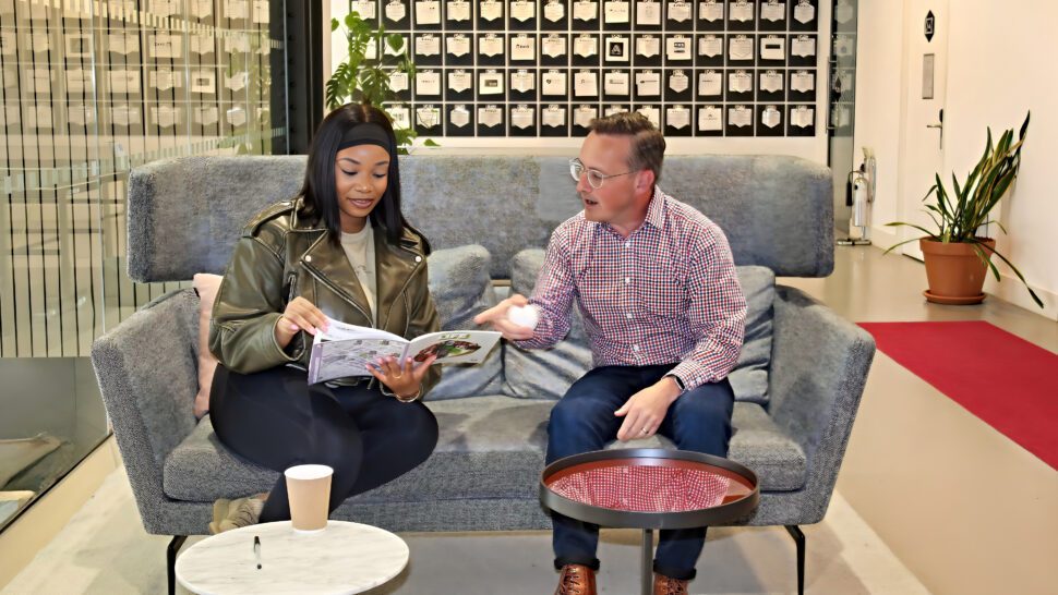 Two people in a discussion sat on a sofa. One of them holds a brochure