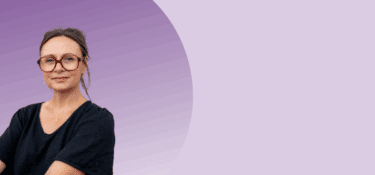 An image of Nancy Doyle wearing a black top posing against a light purple background.