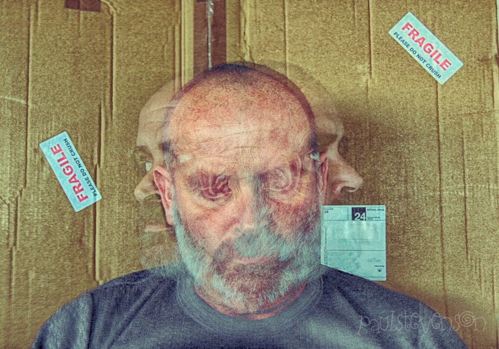 Artistic double-exposure portrait of a bald, bearded man with his head facing forward and in profile to both sides, overlaid on a cardboard box background labeled with red ‘FRAGILE – Please Do Not Crush’ stickers, evoking themes of vulnerability and introspection.
