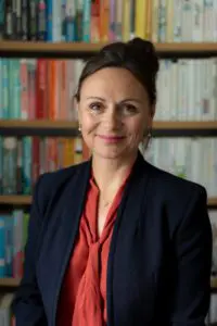 profile photo of Dr Nancy Doyle - she has a library of books in the background. The shot is head and shoulders. She is smiling and wearing a red shirt under a dark blue black jacket.
