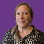 Professional headshot of a woman with blonde hair tied to one side, wearing a black and beige patterned blouse and gold earrings, against a purple background.