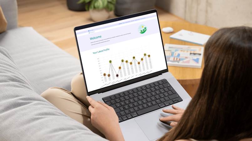 An image of a lady with brown hair holding a laptop on her lap which sat on a sofa. The laptop displays the Genius Finder spiky profile.