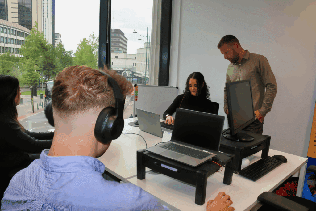 Photo of colleagues working in an open plan office. One male is wearing heaphones.