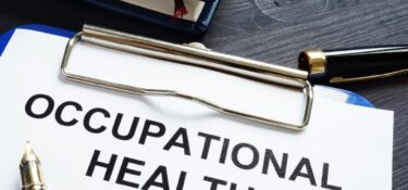 Clipboard with a document titled 'OCCUPATIONAL HEALTH' in bold letters, accompanied by a fountain pen and a closed blue notebook with a red bookmark, placed on a dark wooden surface
