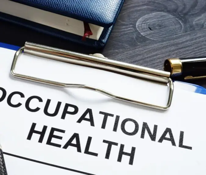 Clipboard with a document titled 'OCCUPATIONAL HEALTH' in bold letters, accompanied by a fountain pen and a closed blue notebook with a red bookmark, placed on a dark wooden surface