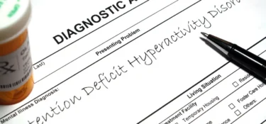 A diagnostic form noting “Attention Deficit Hyperactivity Disorder” with a pen and pill bottles nearby.