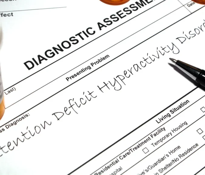 A diagnostic form noting “Attention Deficit Hyperactivity Disorder” with a pen and pill bottles nearby.