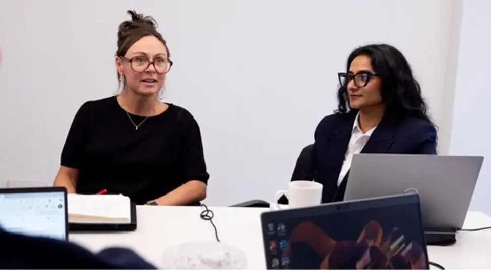 Three people at a table talking with laptops open