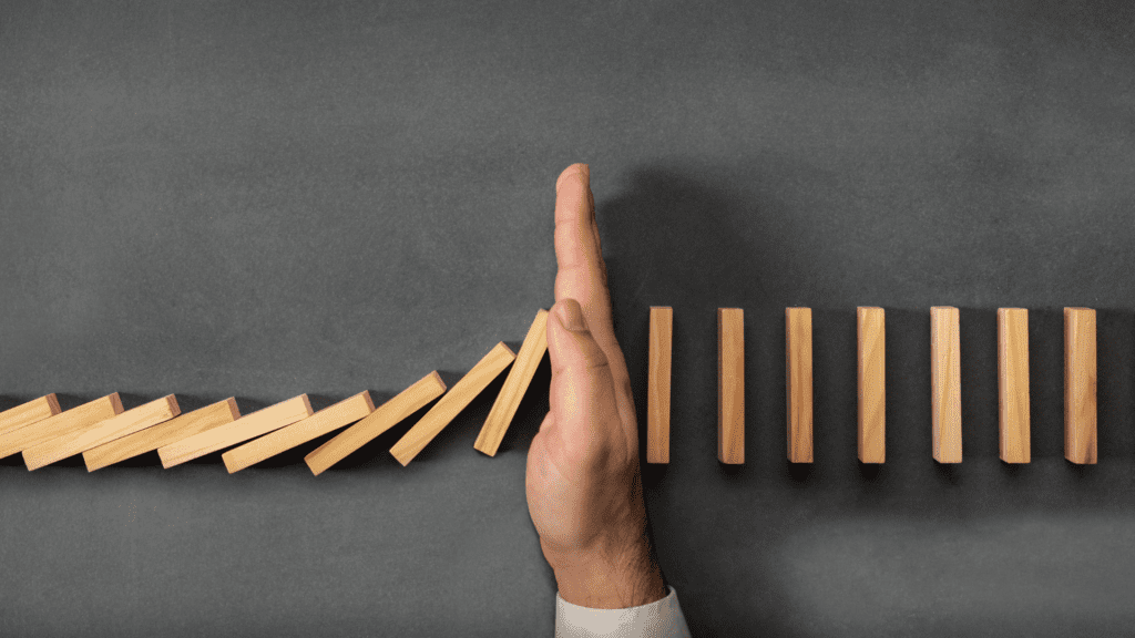 hand blocking a row of dominoes preventing them from collapsing