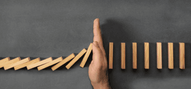 hand blocking a row of dominoes preventing them from collapsing