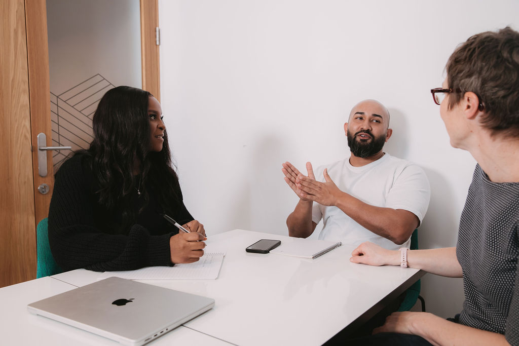 3 people sat at an office table talking