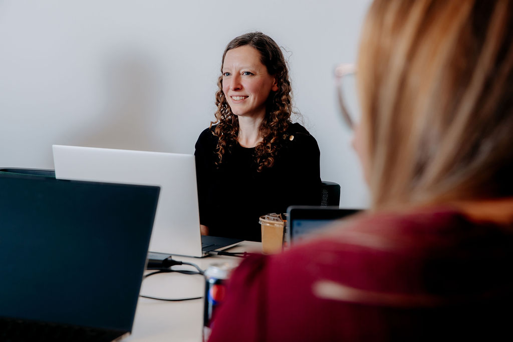 Image shows Helen working remotely with a colleague. She is smiling and wearing a black top