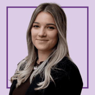 Head-and-shoulders portrait of Courtney Avery smiling with long, centre-parted blonde hair with darker roots, wearing a black blazer over a dark top and a silver necklace. They are looking at the camera against a light purple background with a dark purple square outline behind them.