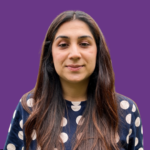Head-and-shoulders portrait of Hirra Khan with long dark brown hair, wearing a navy blue top with large white polka dots. She is looking directly at the camera with a gentle smile. The background is dark purple.