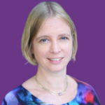 Head-and-shoulders portrait of Nina Strauss, with short blonde hair and a warm smile. She is wearing a colourful blue and pink patterned top with a delicate necklace, against a solid purple background.
