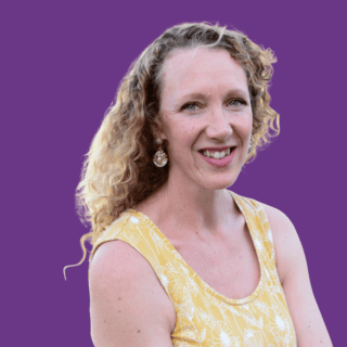Portrait of coach Aleigh Sydenham smiling, with long curly blonde hair, wearing a yellow floral sleeveless top against a purple background.