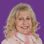 Portrait of Genius Within coach Miranda Pretorius smiling at the camera, with blonde hair and wearing a pale pink top and pink-and-white scarf, against a purple background.