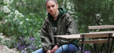 A photo of Whitney Iles sitting in front of green trees.